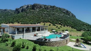 A villa with a swimming pool, outdoor seating, and a view of a mountainous landscape.