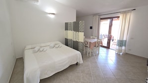 Une chambre avec un lit, une petite table, des chaises, un mur décoré et une porte-fenêtre coulissante donnant sur un espace extérieur.