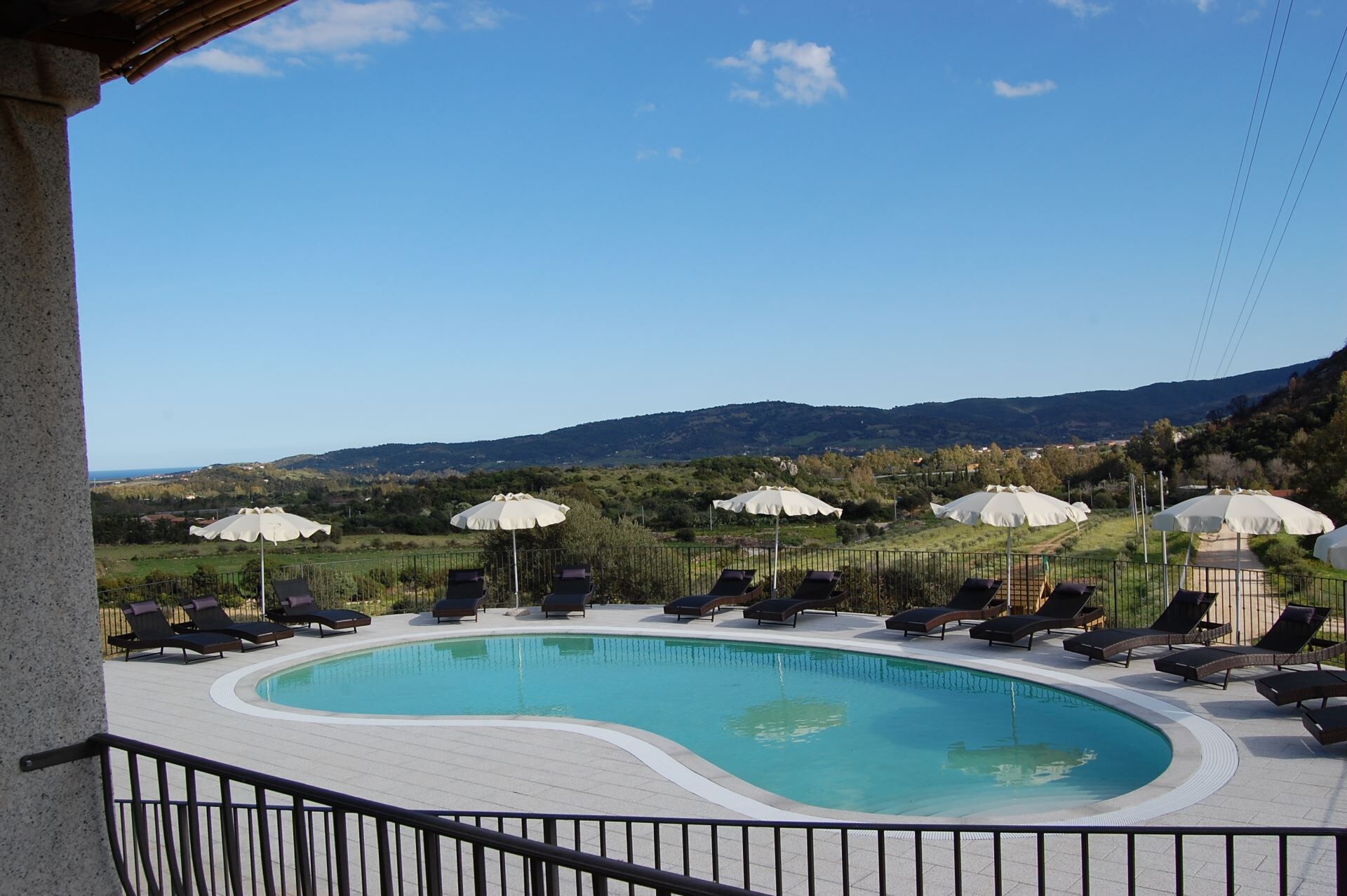 Un espace piscine doté de chaises longues et de parasols, entouré d’une clôture, et offrant une vue sur un paysage montagneux en arrière-plan.