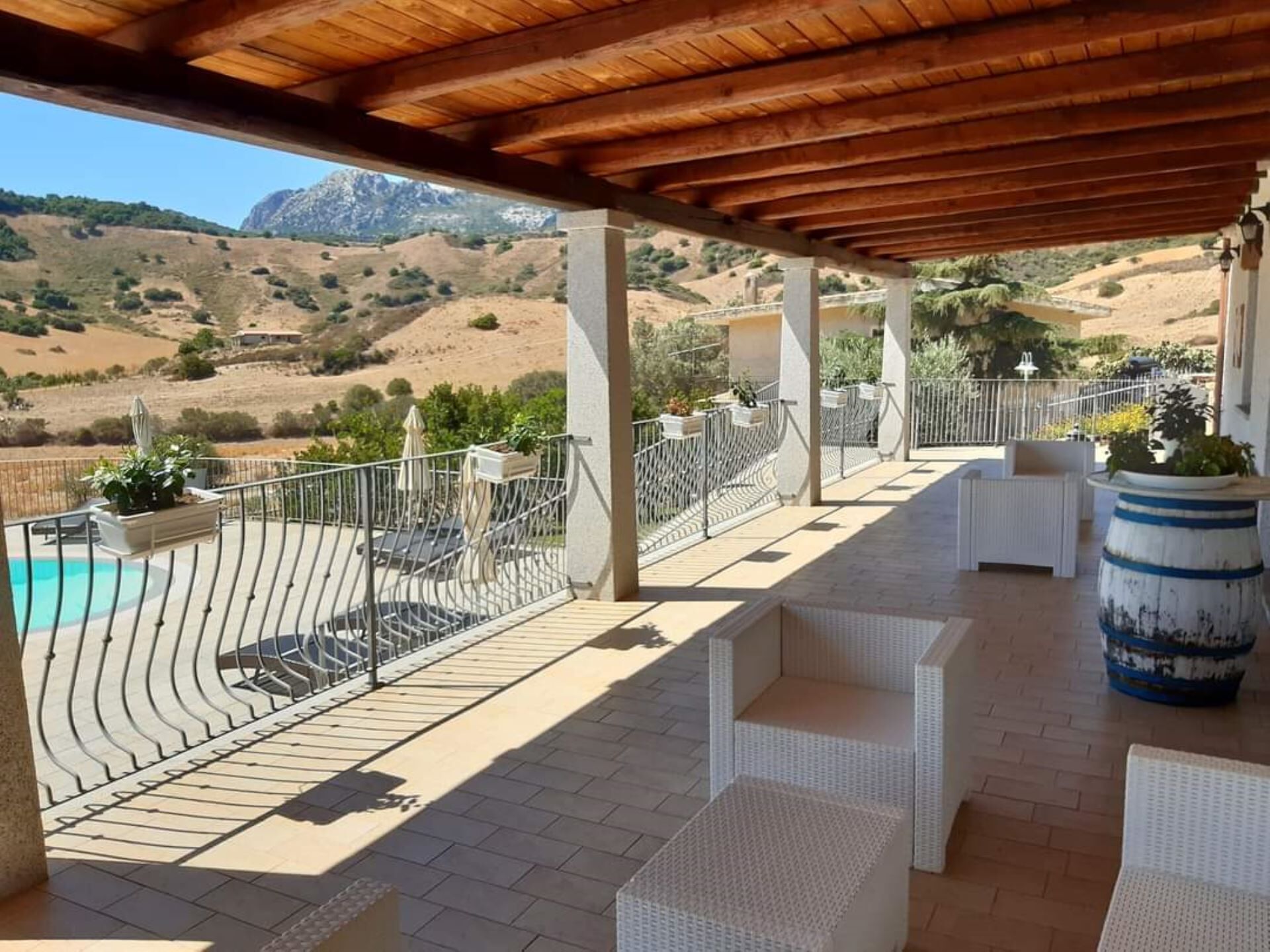 A covered outdoor area with a pool, white wicker furniture, and a view of the hills.