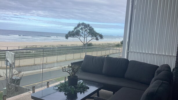 Uma varanda com vista para a praia, um sofá, uma mesa com uma planta e um corrimão.
