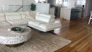 Uma sala de estar moderna com um sofá de couro branco em formato de canto, uma mesa de centro redonda com uma tigela decorativa e um tapete tecido.