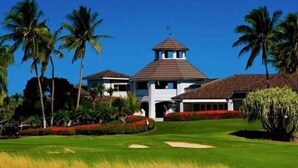 Un parcours de golf doté d’un club-house, de palmiers et surplombé d’un ciel bleu azur.