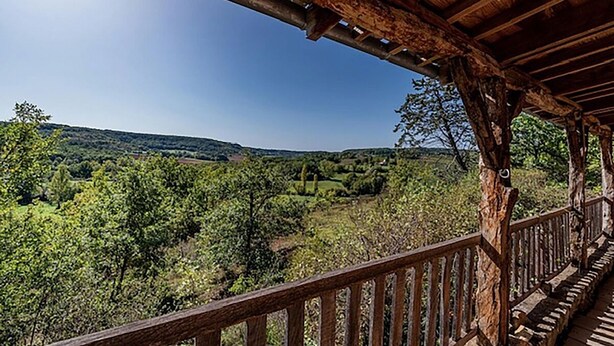Un balcón de madera con vistas a un paisaje verde y exuberante y colinas a lo lejos.