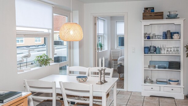 A dining area with a white table and chairs, a hanging light fixture, and a view of the street outside.