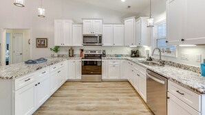 A modern kitchen with white cabinets, granite countertops, stainless steel appliances, and pendant lighting. - Serene Oak Island Home w/ Private Saltwater Pool! (Oak Island)