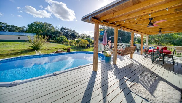 Una terraza de madera con piscina, mobiliario exterior y un área cubierta con ventiladores de techo.