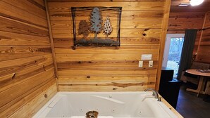 A wooden cabin with a large wooden bathtub, a framed picture of trees, and a small table with chairs.