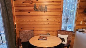A wooden cabin interior with a round wooden table and two wicker chairs.