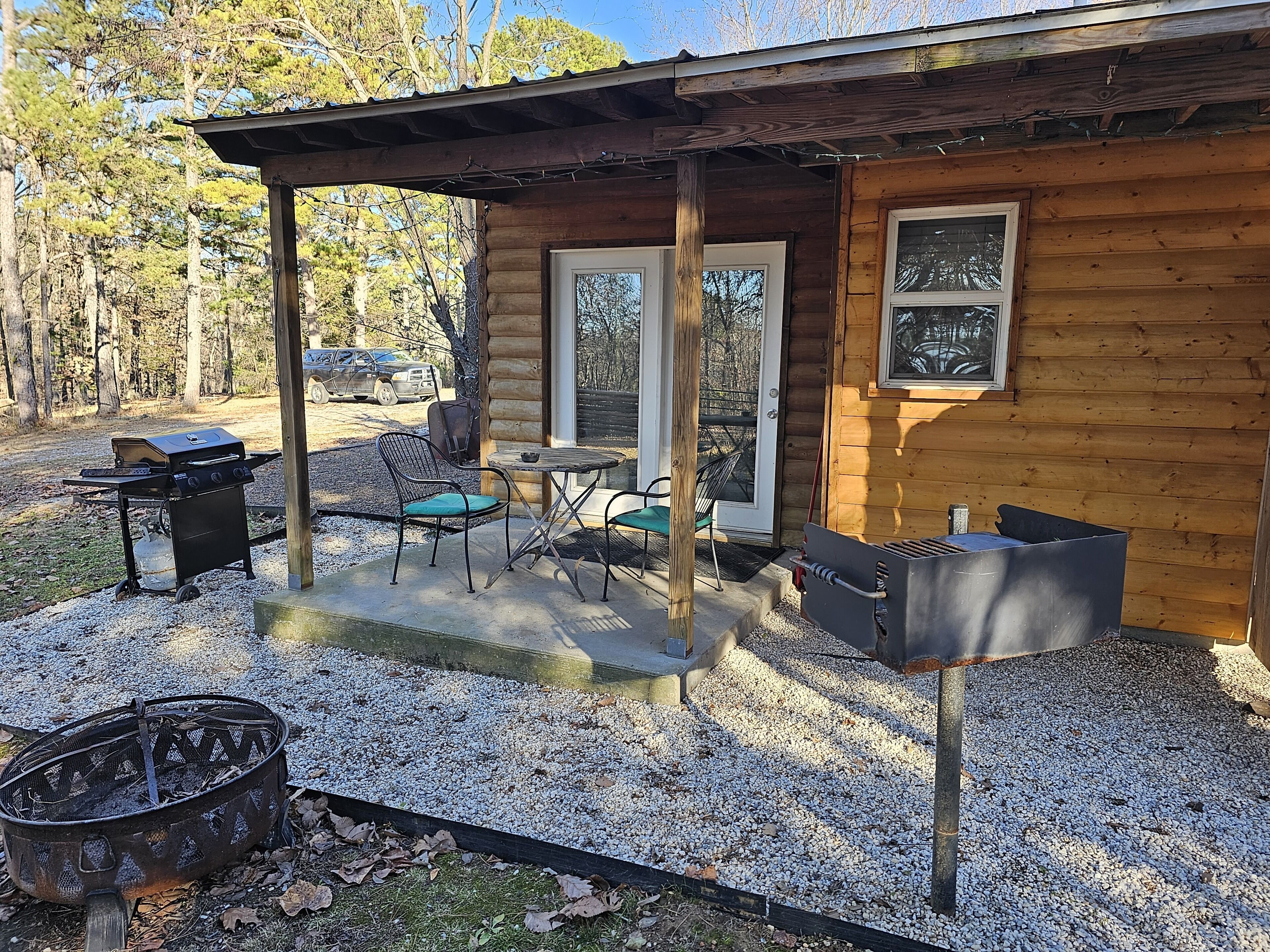 En træhytte med en overdækket terrasse, grill og udendørs møbler.