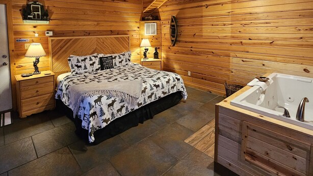A cozy log cabin bedroom with a bed, a large window, a ceiling fan, and a wooden bathtub.