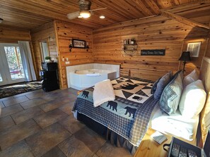 Una habitación estilo cabaña de troncos con una cama grande, una bañera y techo de madera.