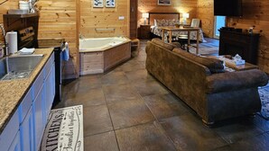 A cozy log cabin interior with a kitchen, a living area with a sofa, a fireplace, and a large bathtub.