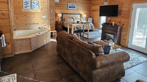 A cozy wooden cabin interior with a bathroom, a living area with a sofa, a dining table, and a fireplace.