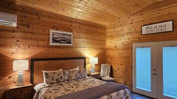 A cozy wooden cabin bedroom with a bed, nightstands, a ceiling fan, and a sign that says "this is our happy place."