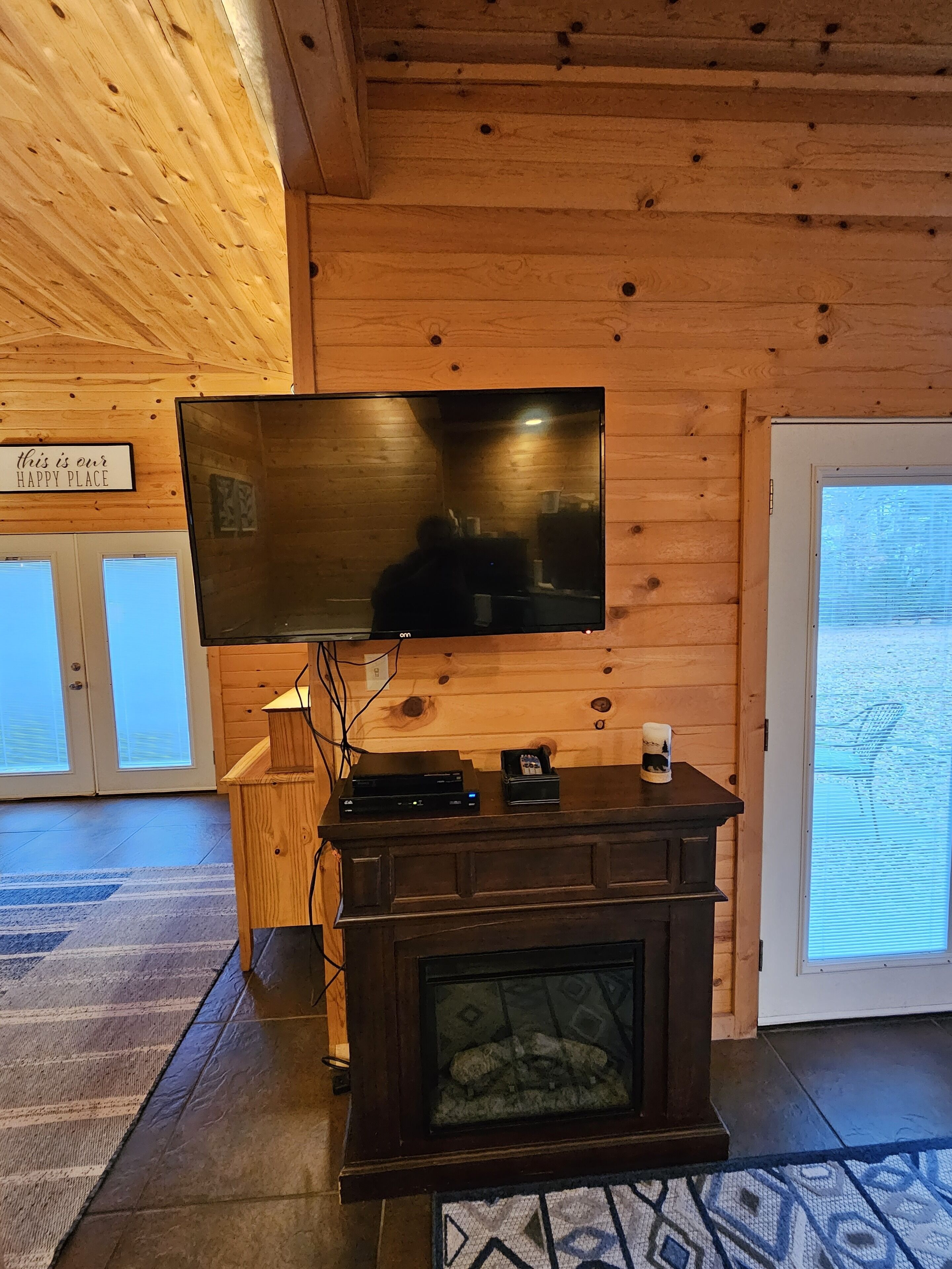 Un interno in legno con una TV a schermo piatto montata a parete, un camino e un cartello con la scritta 'this is our happy place'.