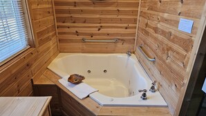 A wooden cabin bathroom with a bathtub, wooden walls, a mirror, and a towel. - Cabin-style private suite: king bed, jetted tub, kitchenette, Wi-Fi & private patio—near Beaver Lake & Eureka Springs. (Eureka Springs)