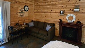 Una habitación acogedora con techo de madera, chimenea, sofá, mesa de comedor con sillas y ventana con cortinas.