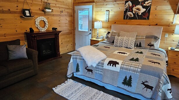Un dormitorio tipo cabaña de madera con una cama, una chimenea, un sofá y techo de madera.