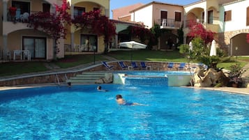 A swimming pool with lounge chairs and a building with balconies and red flowering plants.