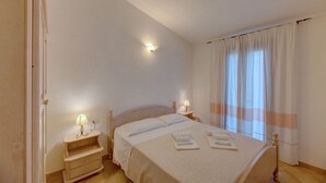 Un dormitorio con cama, lámparas de noche, mesita de noche y ventana con cortinas.