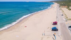 Una playa con una carretera que la recorre, bordeada de coches aparcados y algunas personas caminando.