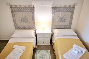 Quarto de hotel com duas camas de solteiro, uma mesa de cabeceira com abajur e um tapete pequeno.