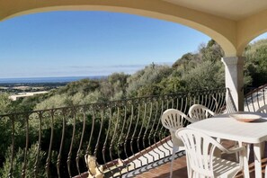 A balcony with a view of the countryside, white outdoor furniture, and a railing.