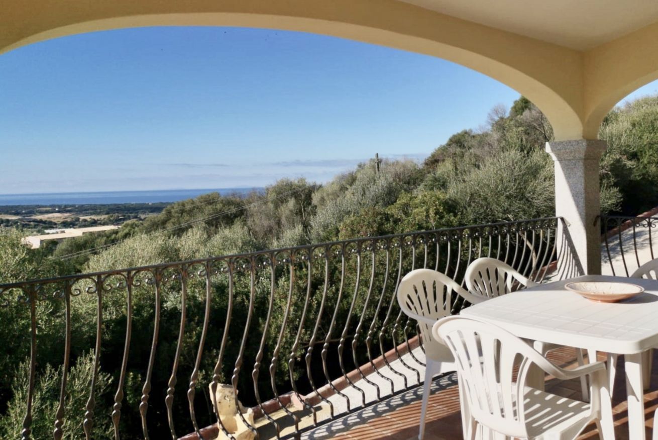 A balcony with a view of the countryside, white outdoor furniture, and a railing.
