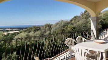 A balcony with a view of the countryside, white outdoor furniture, and a railing.