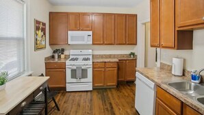 A compact kitchen with wooden cabinets, a microwave, stove, and a dishwasher. - Cozy home perfect for families - Near Naval Base! (Waukegan)
