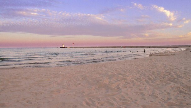 A beach with a lighthouse in the distance, calm waters, and a clear sky. - Cozy home perfect for families - Near Naval Base! (Waukegan)