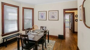 A dining room with a wooden table and chairs, large windows with blinds, and framed artwork on the walls. - Cozy home perfect for families - Near Naval Base! (Waukegan)