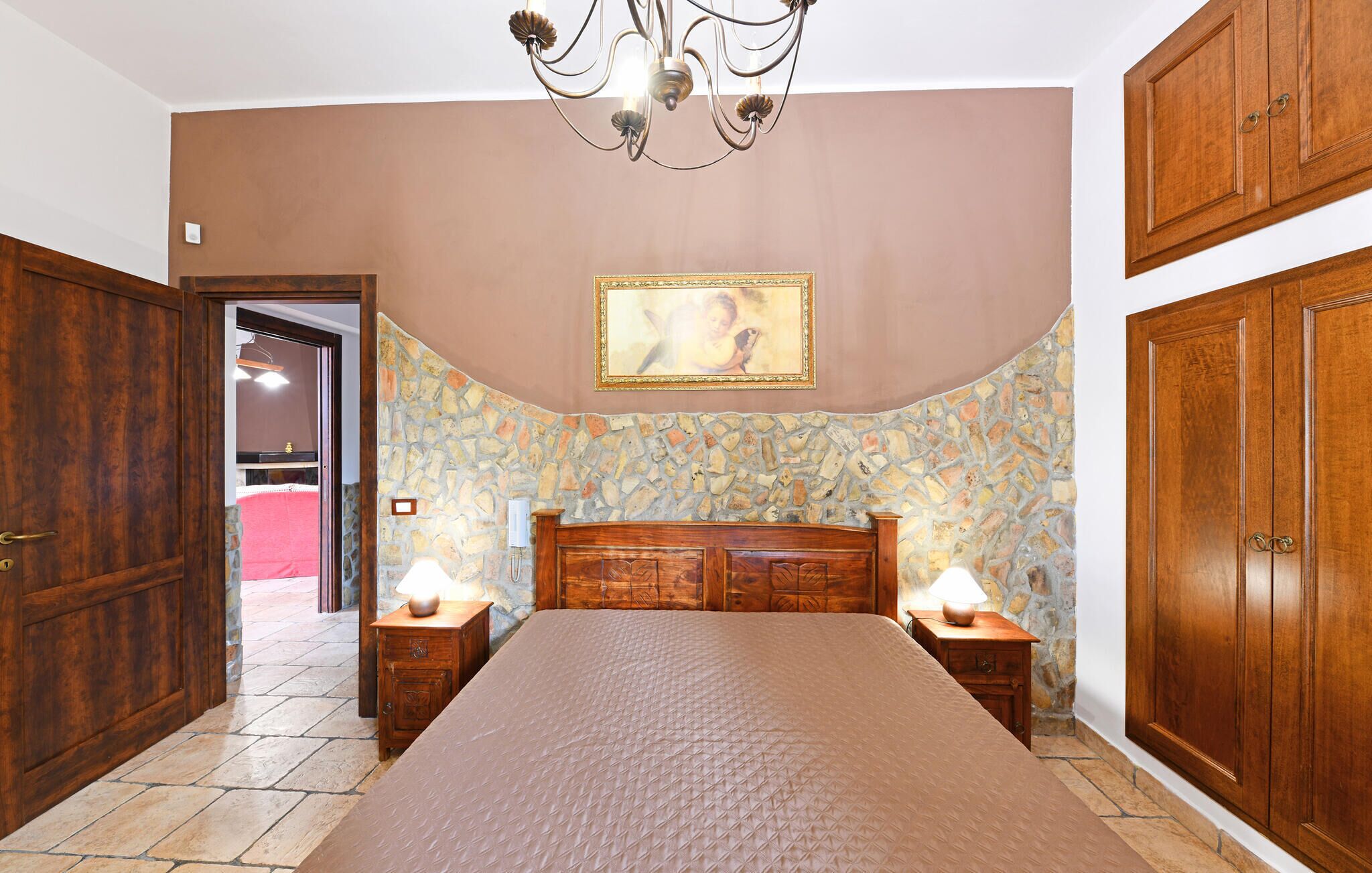 Une chambre avec un grand lit, une armoire en bois et un mur en pierre.