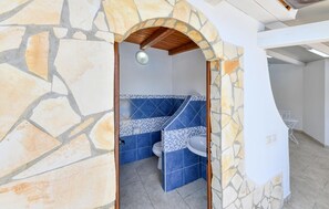 Ein Badezimmer mit Steinwänden, einer gefliesten Dusche und einem weißen Waschbecken.
