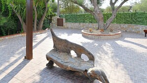Une sculpture d’oiseau, placée sur un banc dans un jardin aux murs de pierre et à la végétation luxuriante.