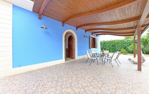 Eine überdachte Terrasse mit Fliesenboden, einem Tisch und Stühlen sowie einer Holztür.