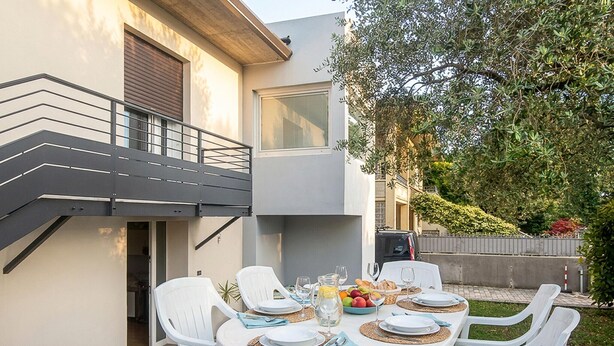 A modern outdoor dining area with a table set for four, surrounded by white chairs, and a staircase leading to an upper level. - Awesome home in Borso del Grappa with house a panoramic view (Borso del Grappa)