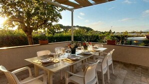 A dining area with a table set for four, surrounded by white chairs, under a pergola with a view of a landscaped garden and distant hills. - 1 bedroom cozy apartment in Massarosa (Massarosa)