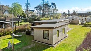 Eine moderne, eingeschossige Holzhütte mit Flachdach, großen Fenstern und einer kleinen Terrasse.