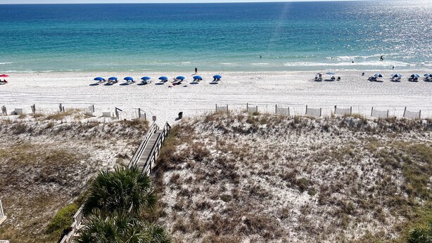 A beach with rows of umbrellas and beach chairs, a sandy shore, and a clear blue ocean. - Renovated oceanfront penthouse condo - direct beach access!  (Fort Walton Beach)