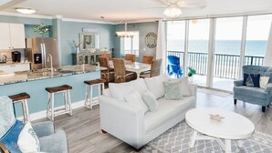 A spacious living area with a sofa, chairs, a dining table, and a kitchen area with a refrigerator and bar stools. - Renovated oceanfront penthouse condo - direct beach access!  (Fort Walton Beach)