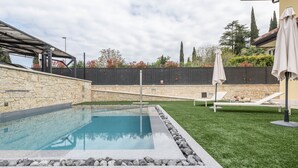 A swimming pool with a stone border, a grassy area, and a pergola structure.