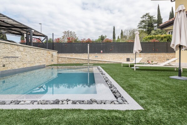 Une piscine bordée de pierres, une pelouse et une structure en forme de pergola.
