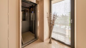 An elevator, a glass door, and a vase with dried plants.