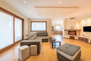 Un salon spacieux comprenant un canapé d’angle, des poufs, une table basse et un téléviseur.