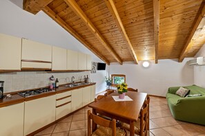 Een keuken met houten keukenkastjes, een eettafel, stoelen, een groene bank en een houten plafond.