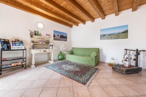 Ein Wohnzimmer mit einem grünen Sofa, einem gemusterten Teppich, einer Holzbalkendecke und einer rustikalen Wasserpumpe.