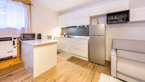 Una cocina compacta con armarios blancos, microondas integrado, refrigerador y un pequeño espacio de asientos.