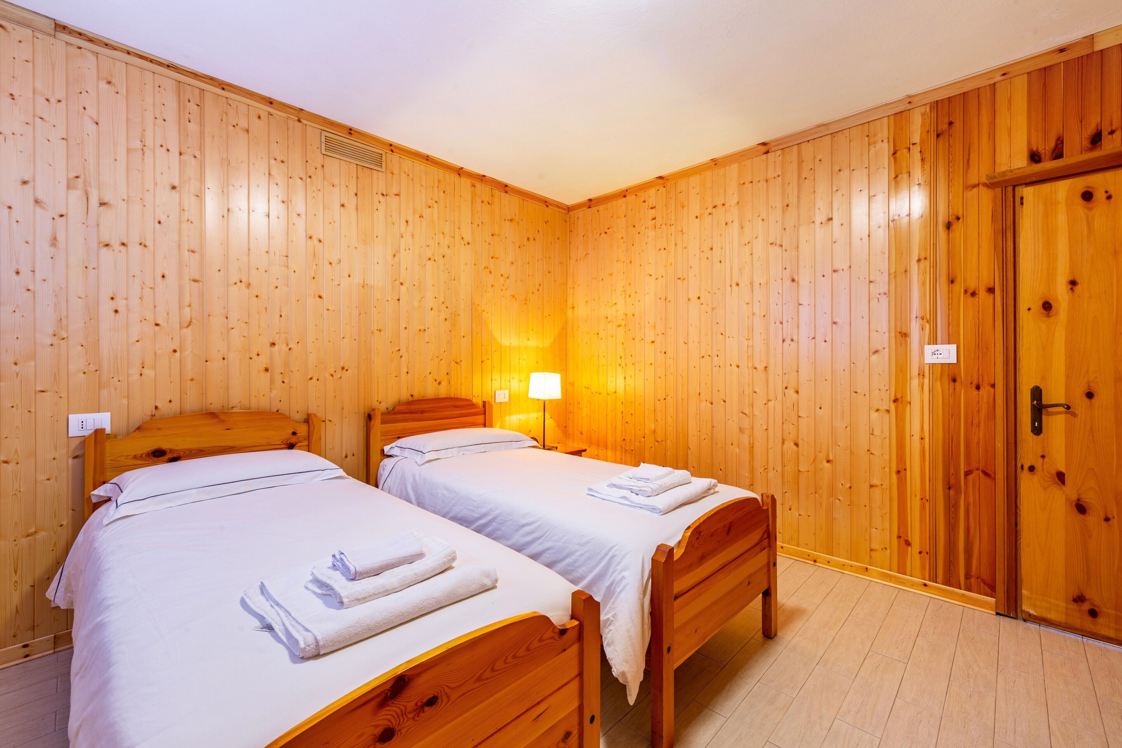 Una habitación con dos camas de madera, una mesita de noche, una lámpara de pared y un armario de madera.